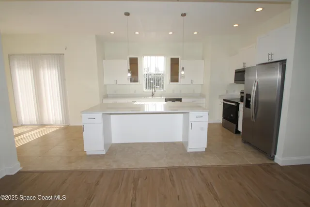 a large kitchen with stainless steel appliances kitchen island granite countertop a large counter top a sink dishwasher a refrigerator and white cabinets next to a window