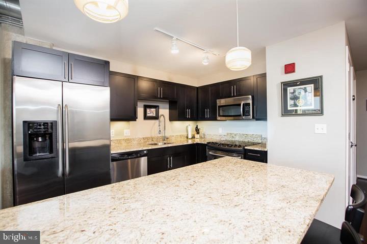 1200 Steuart Street, Unit 428 Baltimore, MD 21230 - Photo 6 of 53 a kitchen with stainless steel appliances kitchen island granite countertop a refrigerator oven a sink with dishwasher and wooden cabinets