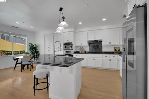 a kitchen with stainless steel appliances granite countertop a refrigerator a sink a stove and a dining table with wooden floor
