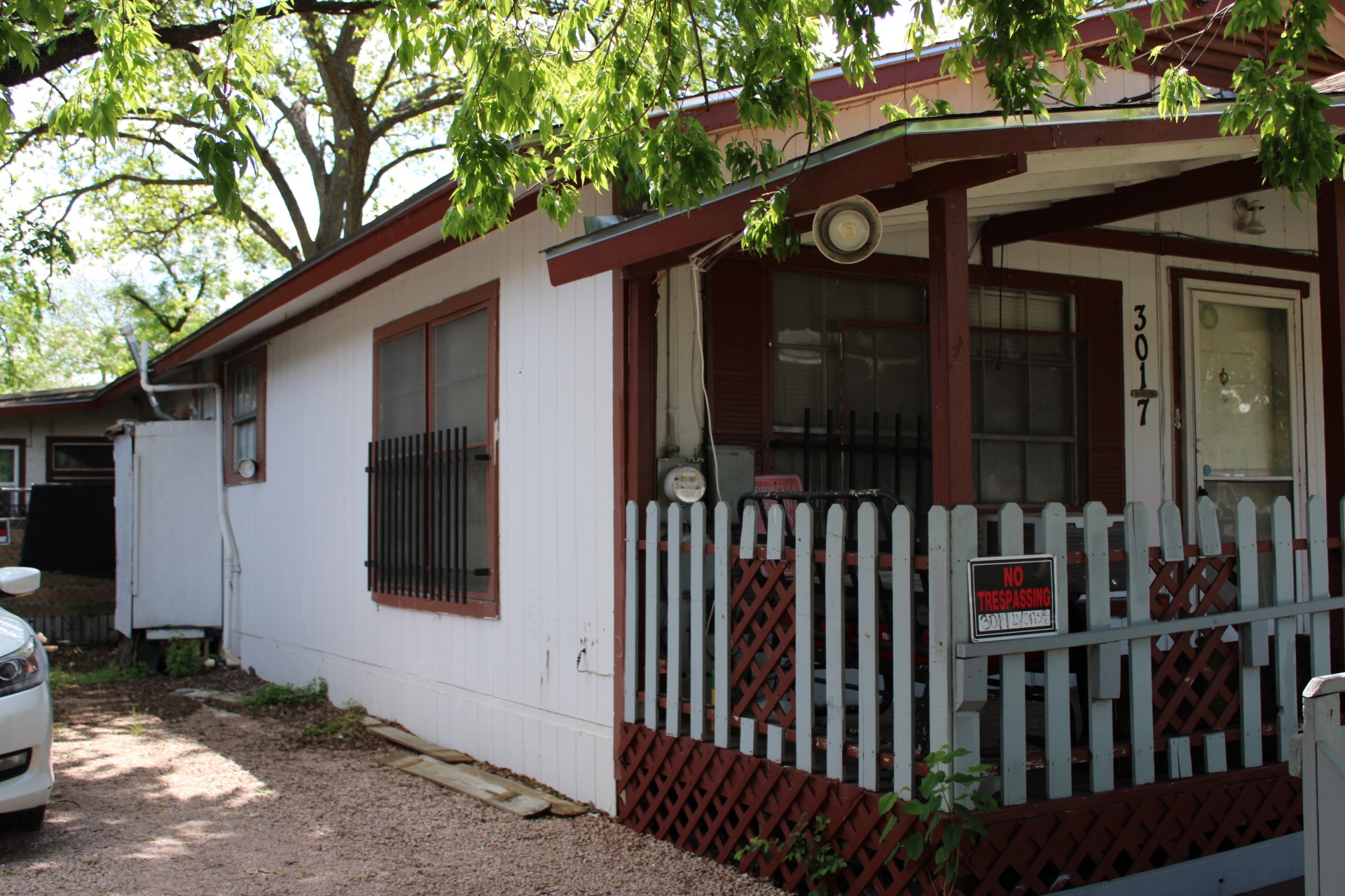 The property features white siding and a covered front porch with a white picket fence and red lattice detailing