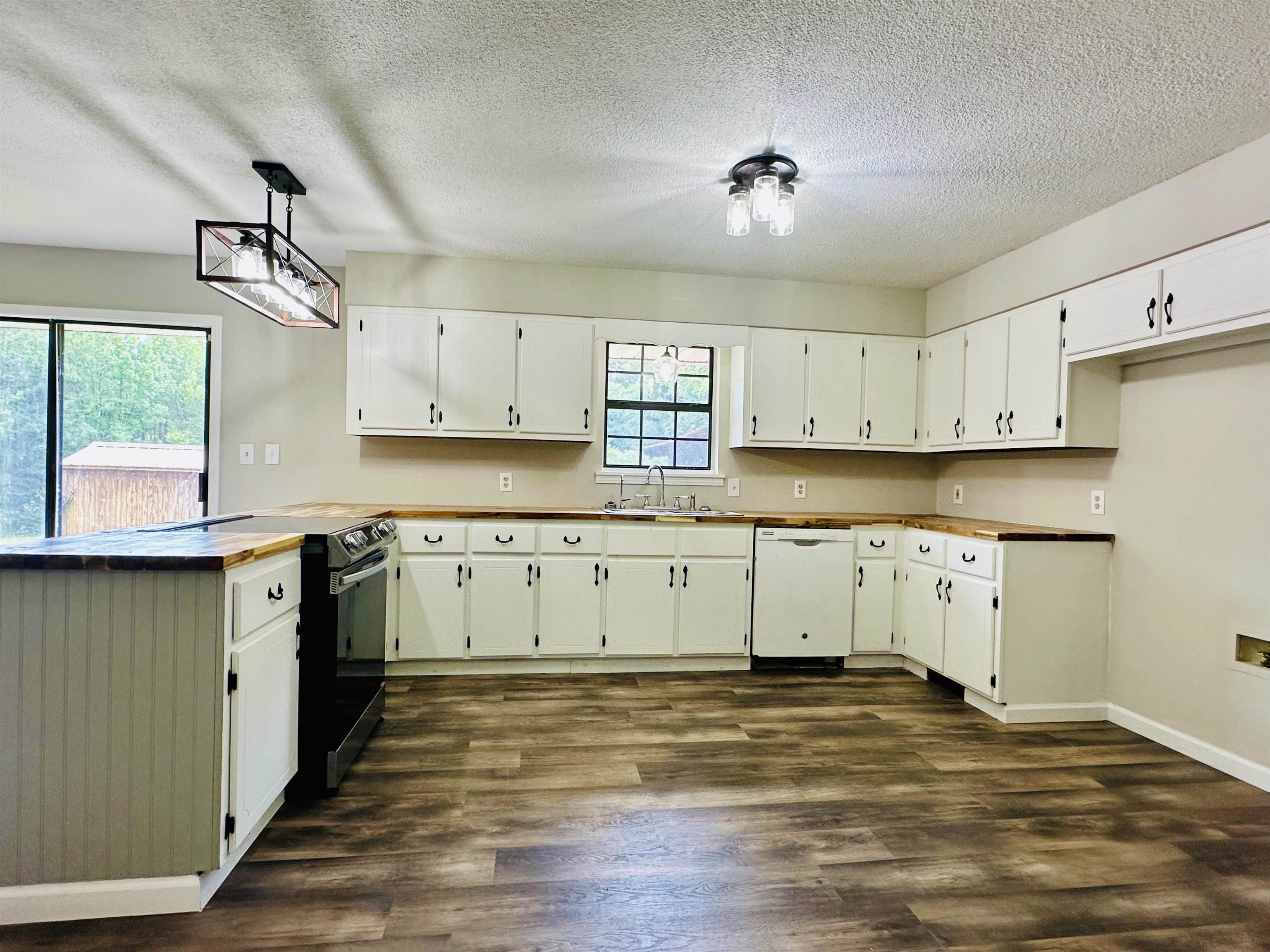 287 Gilchrist Stantonville Road Adamsville, TN 38310 - Photo 19 of 29 Kitchen with a peninsula, a textured ceiling, dark wood-style floors, dishwasher, and white cabinets