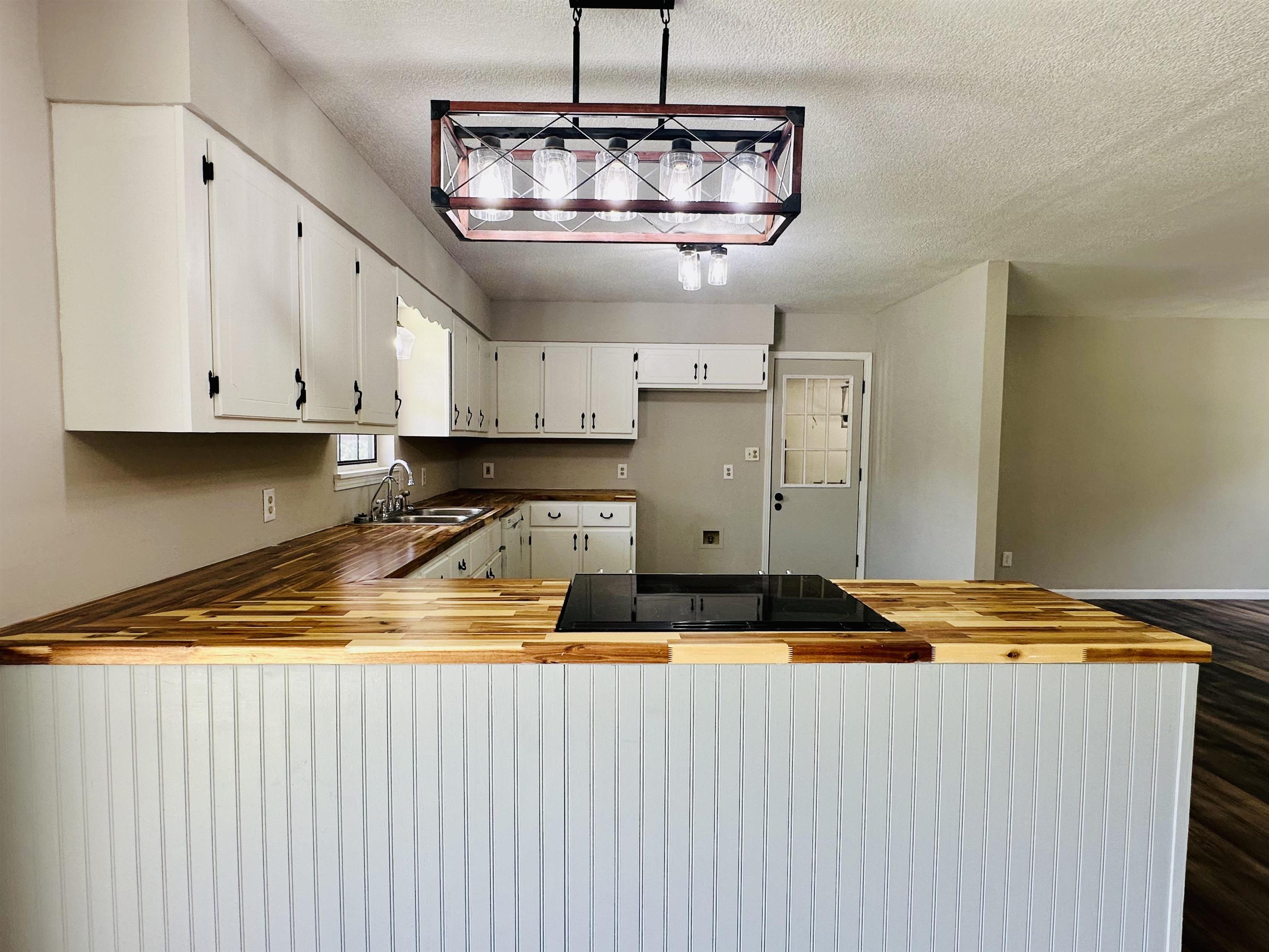287 Gilchrist Stantonville Road Adamsville, TN 38310 - Photo 25 of 29 Kitchen featuring a peninsula, butcher block counters, a textured ceiling, white cabinets, and stovetop
