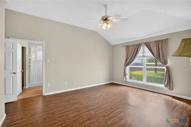 an empty room with wooden floor fan and windows