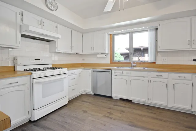 a kitchen with granite countertop white cabinets and white appliances with wooden floor
