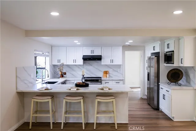 a kitchen with stainless steel appliances kitchen island granite countertop a sink a stove a refrigerator cabinets and chairs