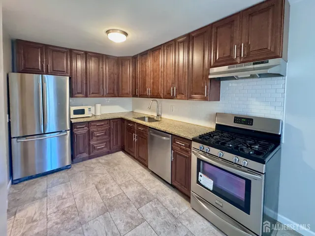 a kitchen with stainless steel appliances granite countertop a stove a refrigerator and a sink with wooden cabinets