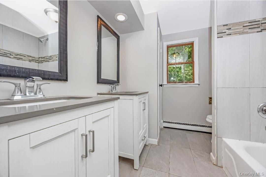 9 Half Moon Pond Road Ridge, NY 11961 - Photo 19 of 26 Dual vanities with integrated sinks and chrome fixtures, grey countertops, tiled flooring, and a tiled shower with a decorative mosaic accent