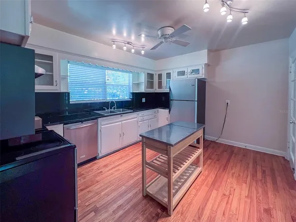 a kitchen with stainless steel appliances granite countertop a sink a stove a refrigerator cabinets and wooden floor