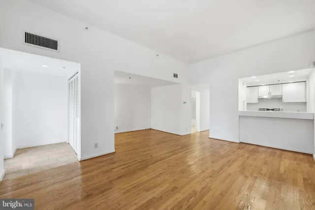 a view of an empty room with wooden floor and a kitchen