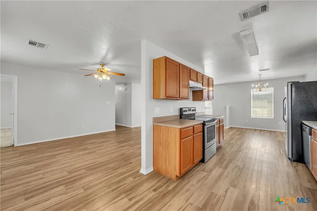 a kitchen with stainless steel appliances granite countertop a stove a sink dishwasher and a refrigerator with wooden floor