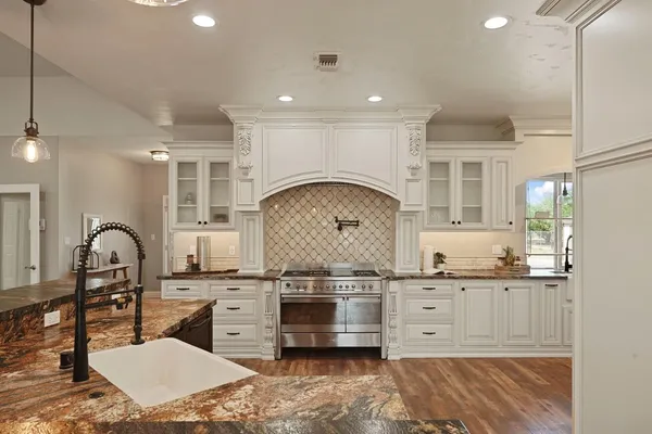 a kitchen with stainless steel appliances kitchen island granite countertop a stove a sink a refrigerator and white cabinets with wooden floor