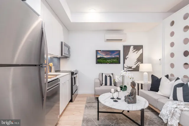 a living room with stainless steel appliances furniture a rug and a kitchen view