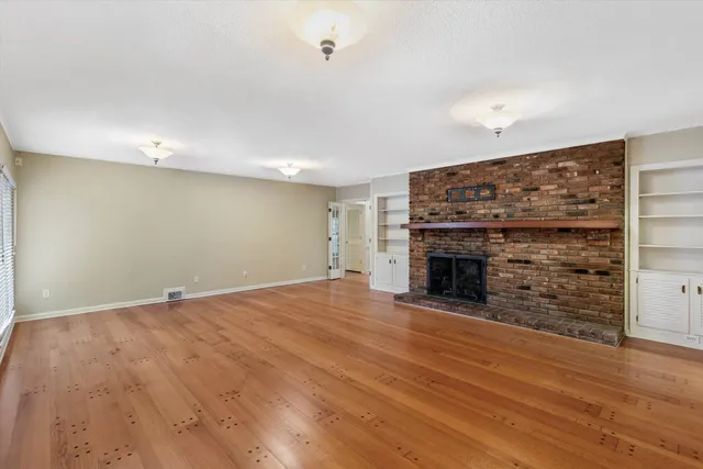 a view of an empty room with wooden floor fireplace and a window