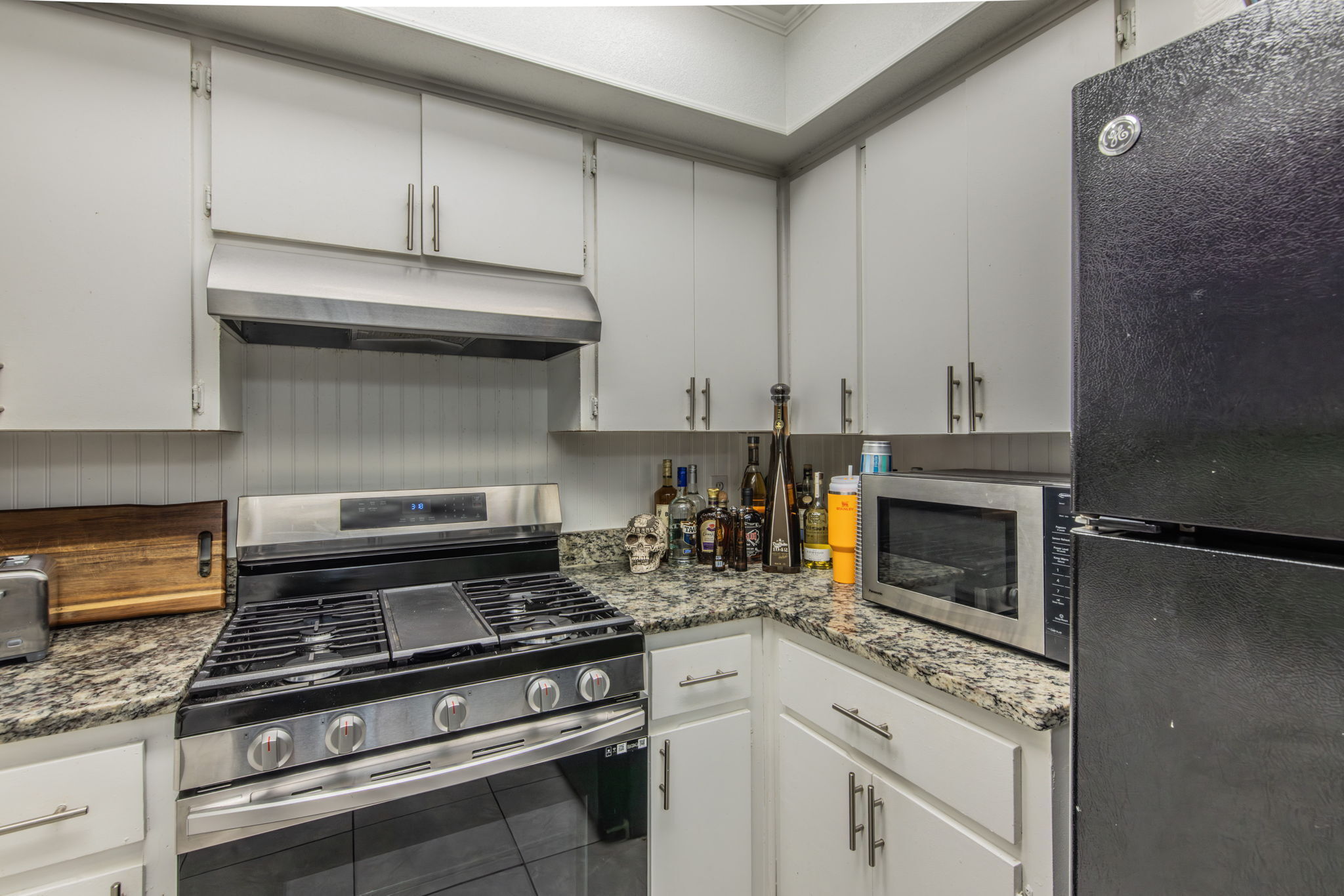 1008 Milford Way Austin, TX 78745 - Photo 27 of 40 Kitchen with white cabinetry, granite-style countertops, stainless steel range with overhead ventilation, and a black refrigerator