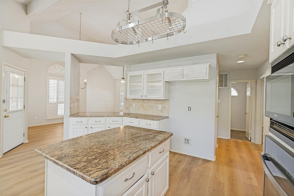 1215 Spring Creek Drive Allen, TX 75002 - Photo 10 of 40 Kitchen featuring a center island with stone countertop, white cabinetry, integrated oven and microwave, wood-finish flooring, and a decorative ceiling pot rack