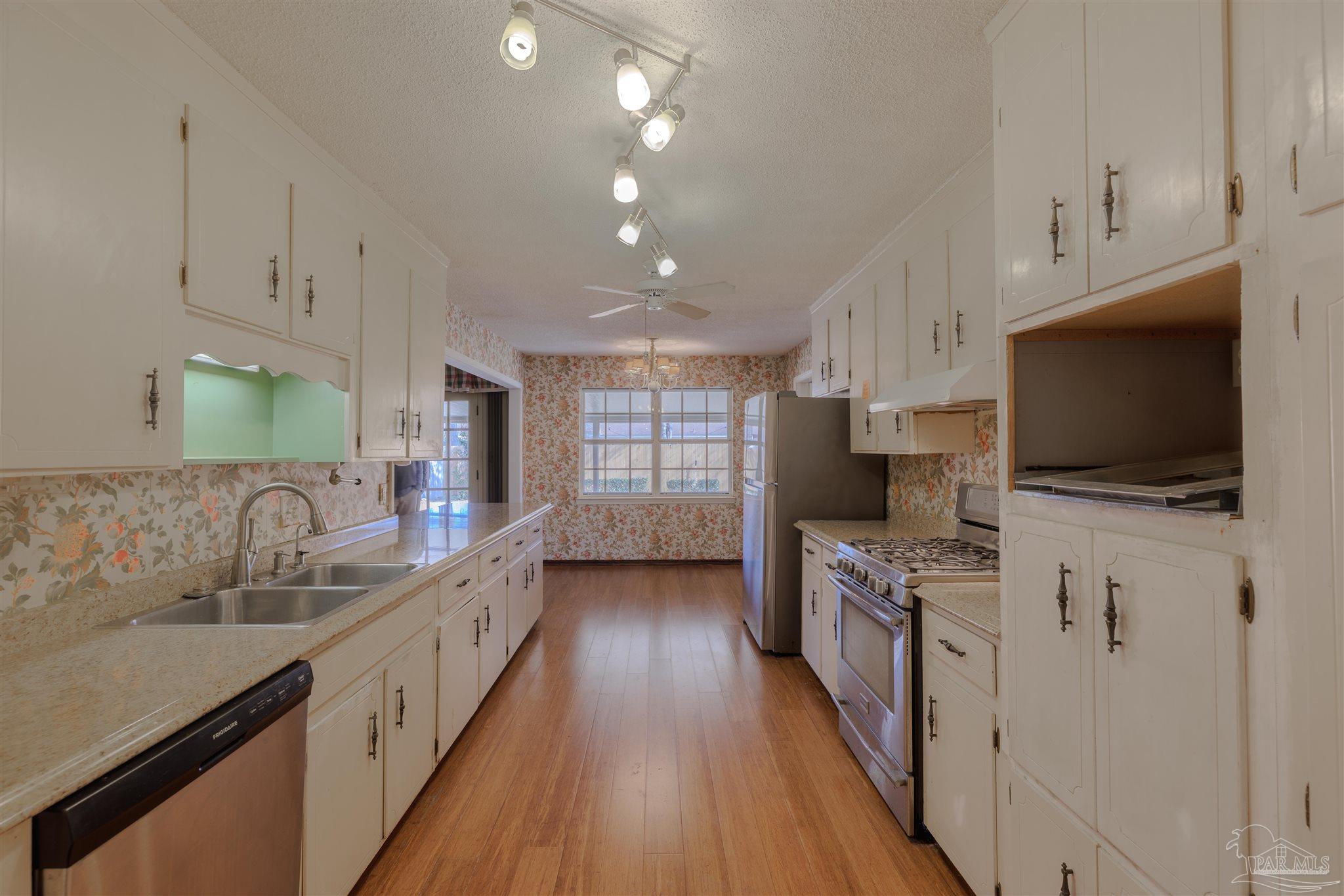 5700 Adelyn Road Pensacola, FL 32504 - Photo 7 of 33 a kitchen with stainless steel appliances a sink dishwasher a stove top oven a refrigerator with grey cabinets and wooden floor