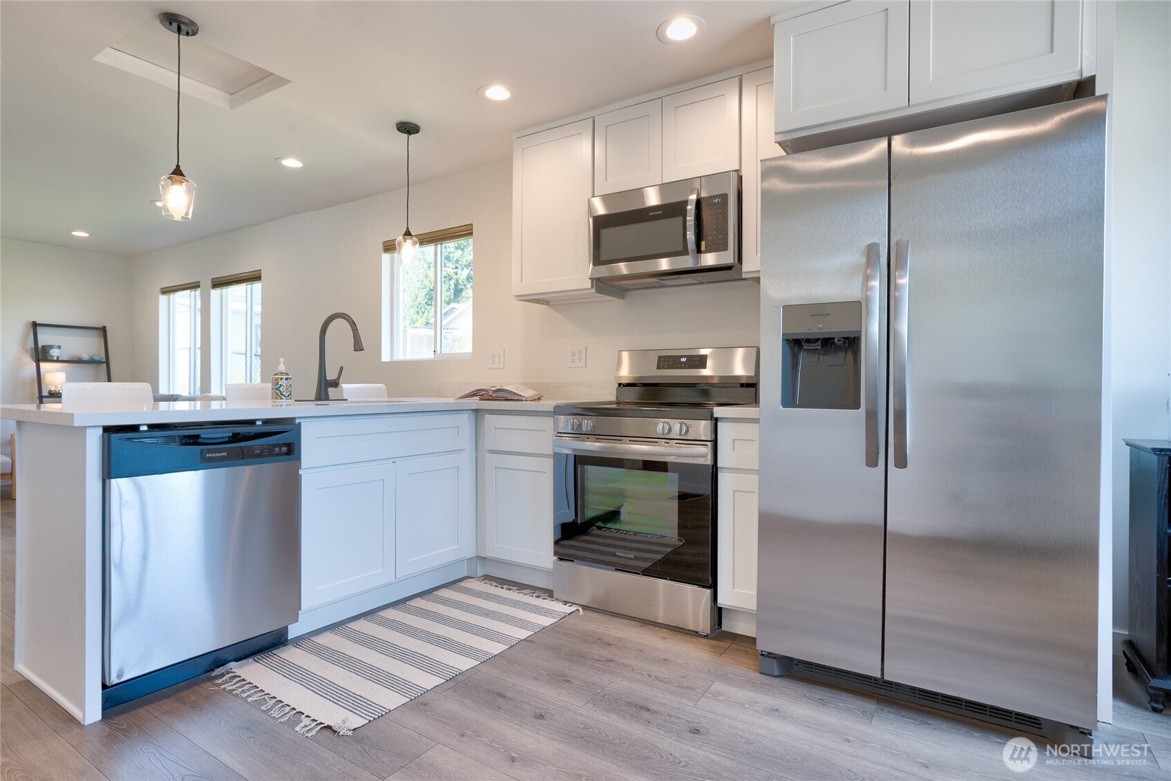 10059 8th Avenue Southwest Seattle, WA 98146 - Photo 4 of 24 a kitchen with stainless steel appliances kitchen island granite countertop a refrigerator a sink a stove and white cabinets with wooden floor