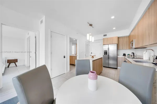a kitchen with stainless steel appliances kitchen island granite countertop a refrigerator a stove a sink a dining table and chairs with wooden floor