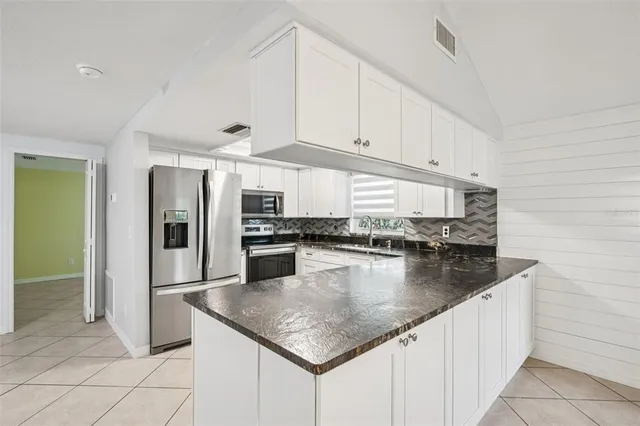 a kitchen with stainless steel appliances granite countertop a refrigerator a sink and white cabinets