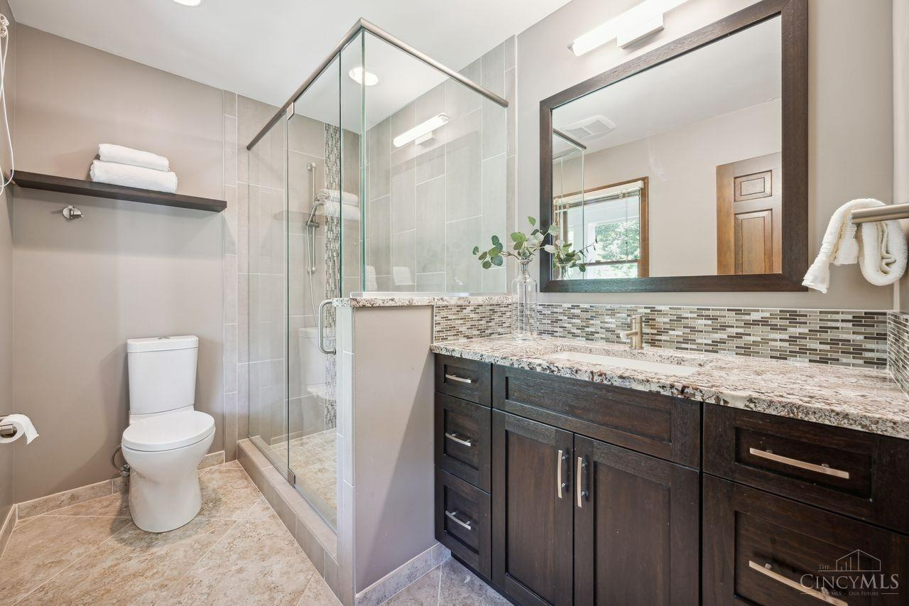 8589 Weller Road Montgomery, OH 45249 - Photo 18 of 30 The primary bath features a new shower with a sleek glass design, wood cabinets topped with granite and a tiled backsplash.