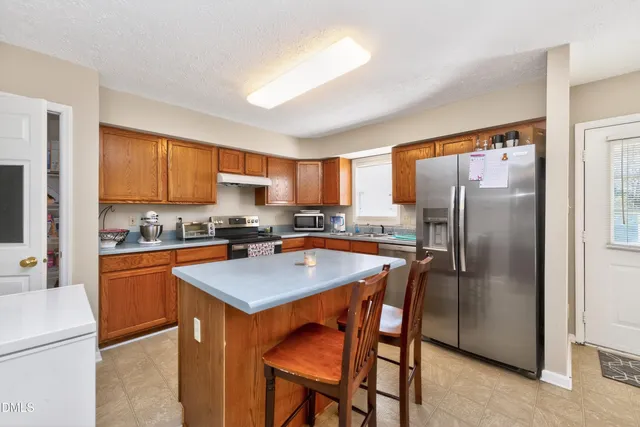 a kitchen with stainless steel appliances granite countertop a refrigerator a sink a stove a dining table and chairs
