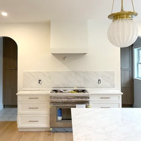 a large white kitchen with granite countertop a stove a sink dishwasher and a refrigerator with wooden floor