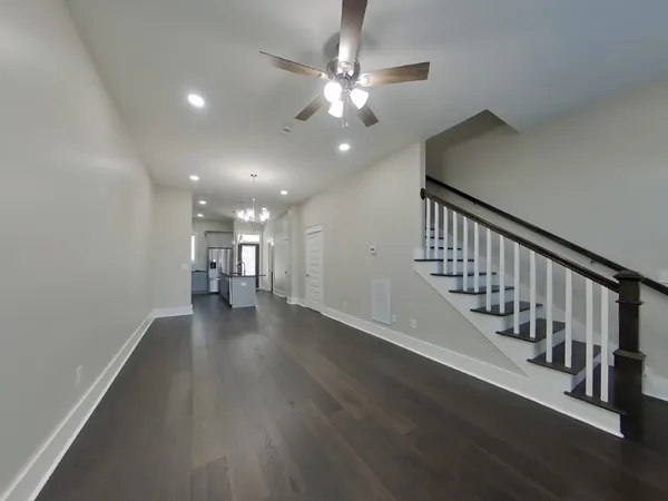 a view of an empty room with wooden floor and a chandelier fan