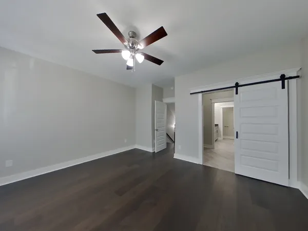 a view of an empty room with wooden floor and a ceiling fan