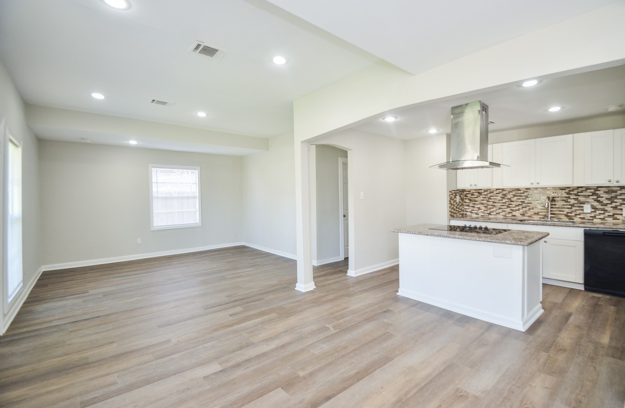 5238 Keystone Street Houston, TX 77021 - Photo 6 of 31 Open-concept living area flowing into a kitchen with white cabinetry, a stylish mosaic backsplash, and a central island with a built-in cooktop, ideal for entertaining.