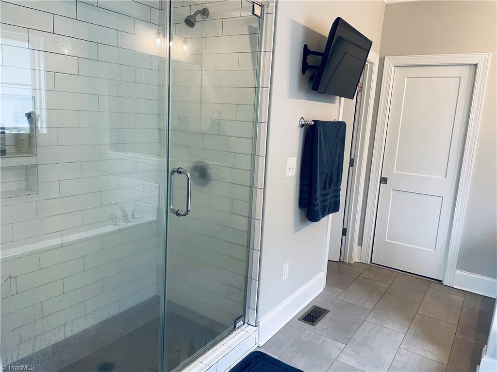 8805 Colgate Road Stokesdale, NC 27357 - Photo 10 of 34 Large bath just off the primary bedroom boast of space with tiled, separate shower, garden tub, two sink areas, TV and large walk in closet