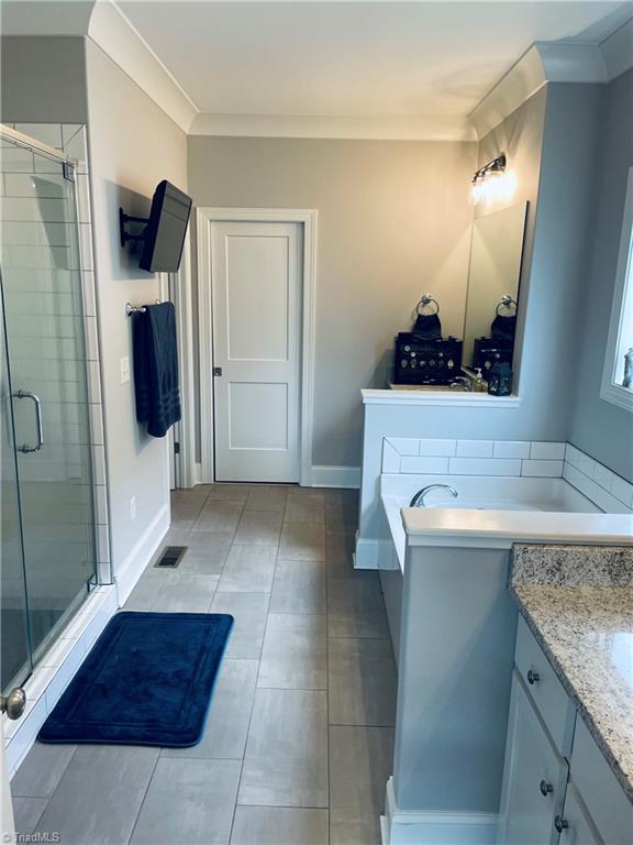 8805 Colgate Road Stokesdale, NC 27357 - Photo 11 of 34 Large bath just off the primary bedroom boast of space with tiled, separate shower, garden tub, two sink areas, TV and large walk in closet