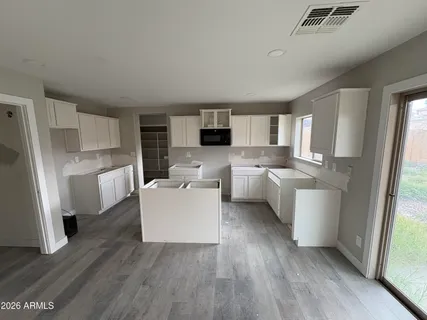 a living room with stainless steel appliances a microwave a refrigerator a sink and white cabinets with wooden floor