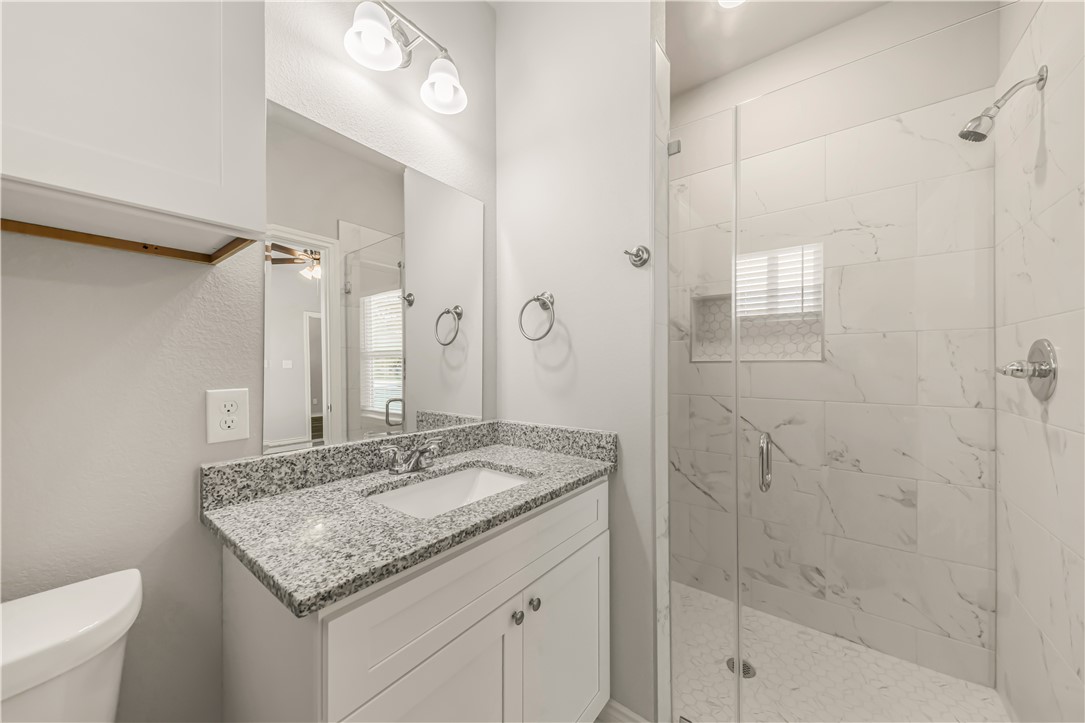 1801 Pin Oak Street Bryan, TX 77803 - Photo 16 of 17 a bathroom with a granite countertop sink a mirror and a shower