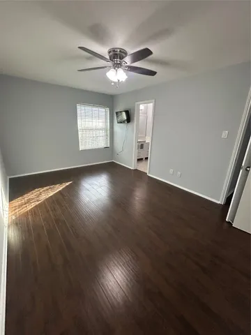 a view of an empty room with wooden floor and a ceiling fan