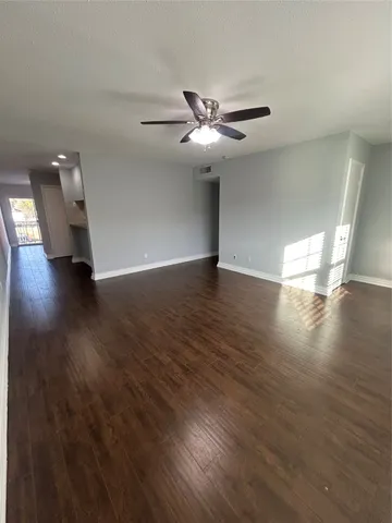 a view of an empty room with wooden floor and a ceiling fan