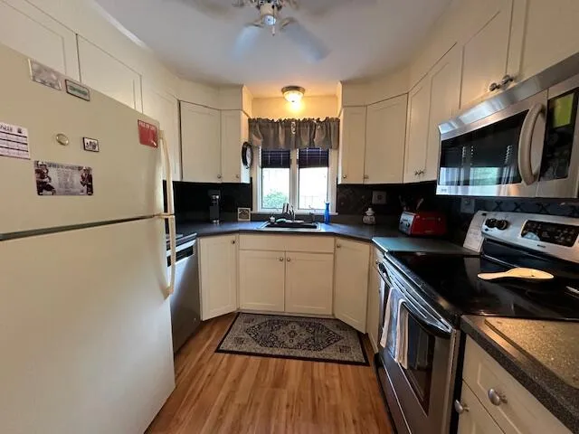 a kitchen with granite countertop a refrigerator a sink dishwasher a stove and white cabinets with wooden floor