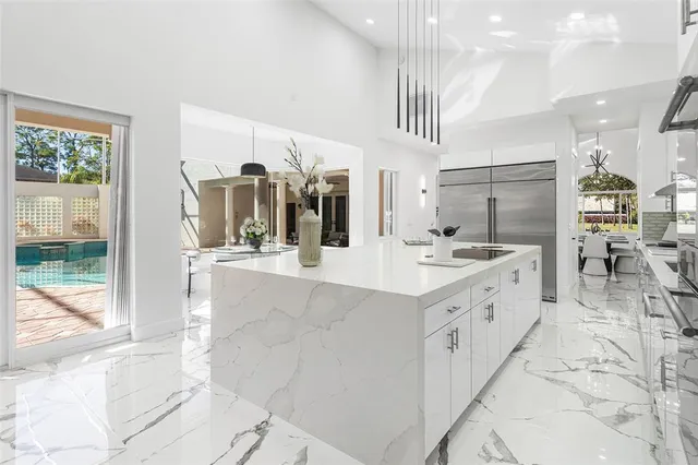 a large white kitchen with kitchen island a large counter top space a sink stainless steel appliances and cabinets