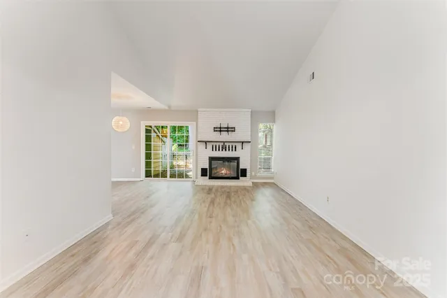 an empty room with wooden floor fireplace and windows