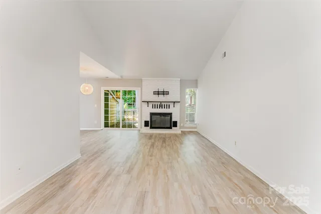 an empty room with wooden floor fireplace and windows