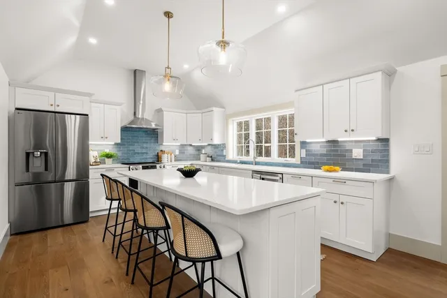 a kitchen with stainless steel appliances a stove a refrigerator a sink a center island and chairs with wooden floor