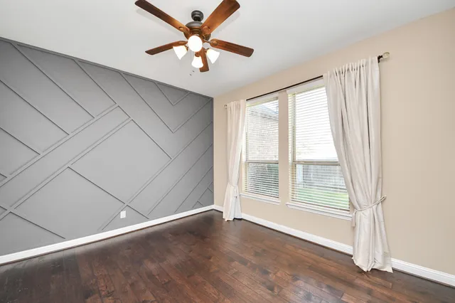 an empty room with wooden floor fan and windows