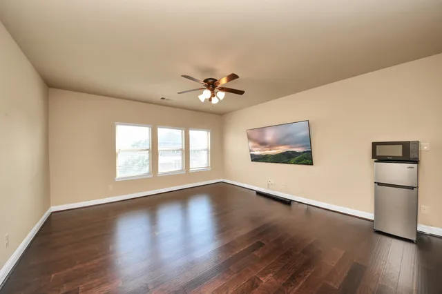 an empty room with wooden floor chandelier fan and windows