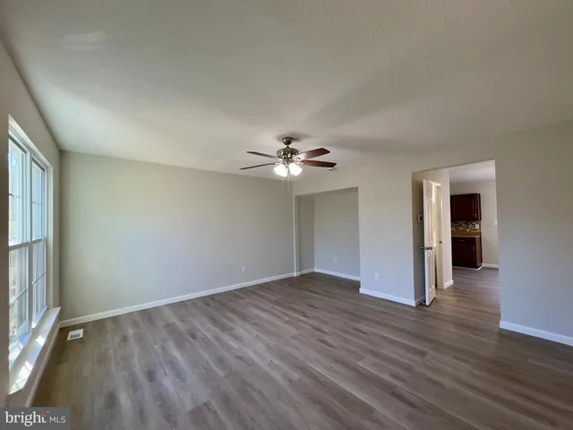 an empty room with wooden floor chandelier fan and windows
