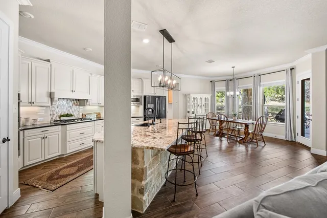 a kitchen with stainless steel appliances granite countertop a stove a refrigerator a kitchen island a dining table and chairs with wooden floor
