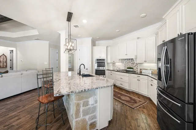 a kitchen with stainless steel appliances granite countertop a refrigerator a sink dishwasher a stove and white cabinets with wooden floor