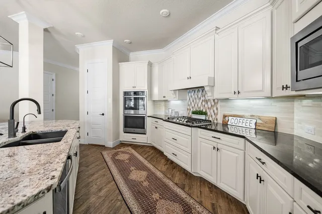 a kitchen with granite countertop a sink stainless steel appliances and white cabinets