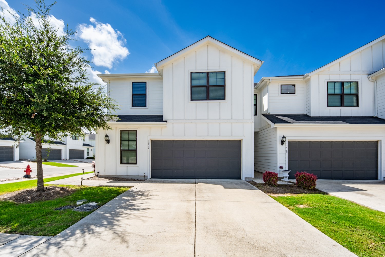 A striking modern facade features crisp white siding, dark trim windows, and a generous driveway leading to an attached garage.