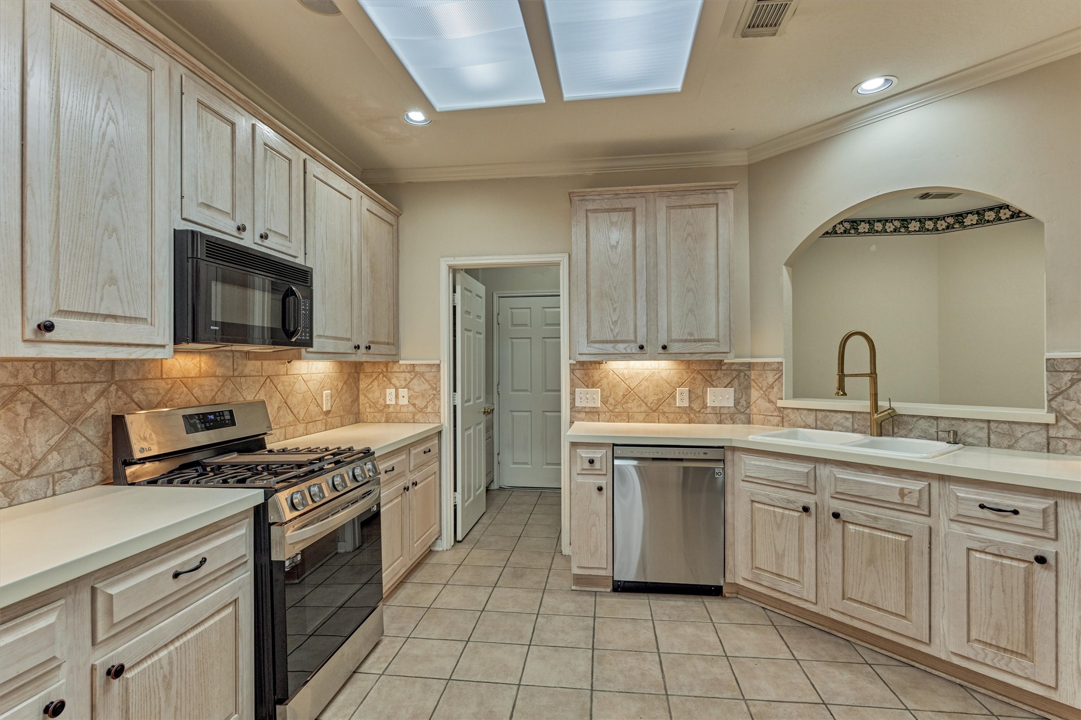 14420 Walters Road, Unit 26 Houston, TX 77014 - Photo 14 of 45 This kitchen features light wood cabinetry, stainless steel appliances, and tiled flooring. It includes a gas stove, built-in microwave, and a dishwasher. The space is accented with a tile backsplash and illuminated by recessed lighting and skylights.