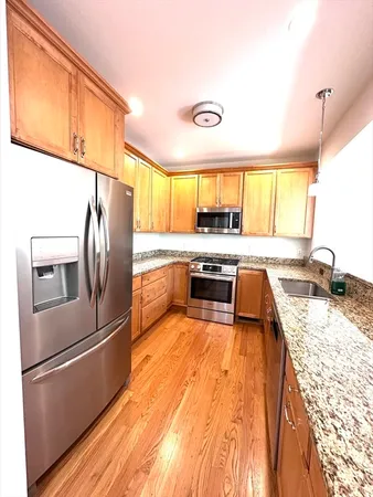 a kitchen with stainless steel appliances granite countertop a refrigerator a sink dishwasher a stove and a dining table with wooden floor