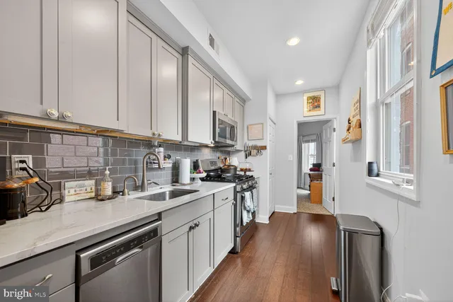 a kitchen with stainless steel appliances granite countertop a stove top oven a sink a refrigerator white cabinets and wooden floor